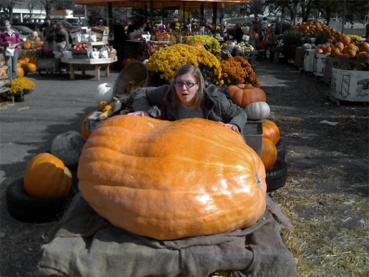 woman in glasses laying on large pumpkin shaped object at farmers market