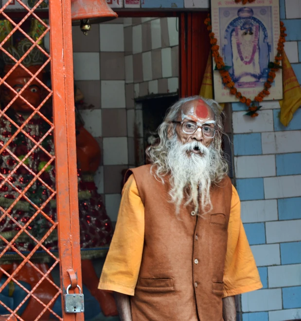 old man with white beard and big beard standing outside a temple