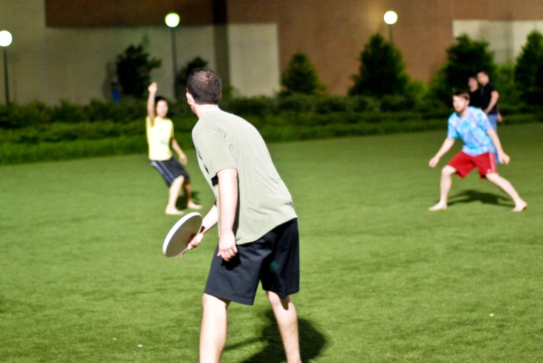 people playing with frisbees on a field in front of a building at night