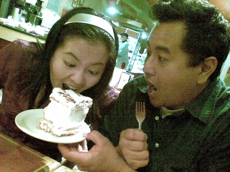 a man and woman eating from forks together at a table