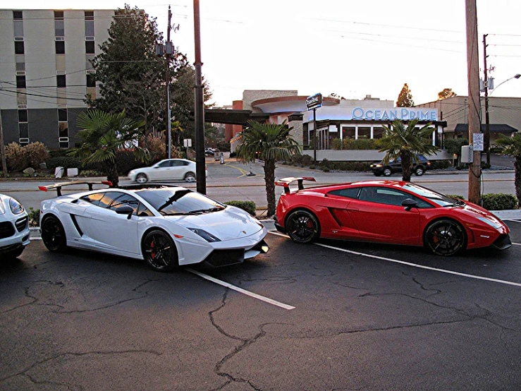 two sports cars, one white and one red, are parked in a lot
