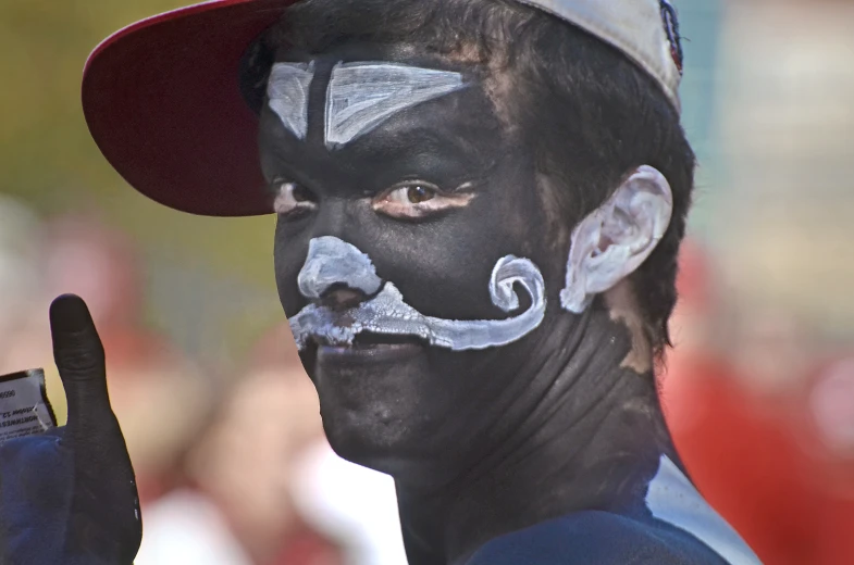 a person wearing face paint and a hat holding a cigarette