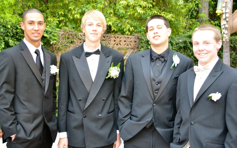 four men in black tuxedos standing together