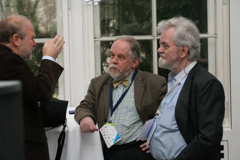 three men talking in front of some windows