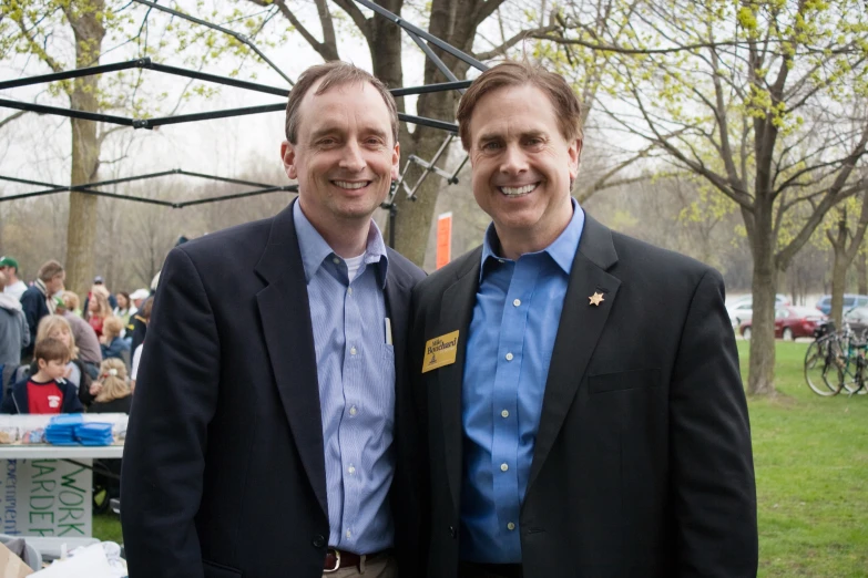 two men smiling while standing in a park