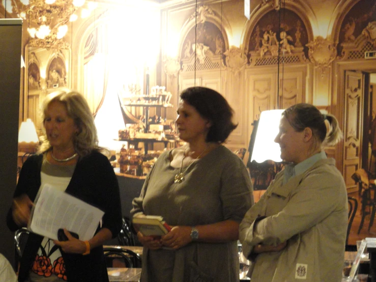 three women stand side by side talking in a room