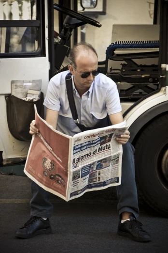 a man is sitting reading the newspaper while looking down
