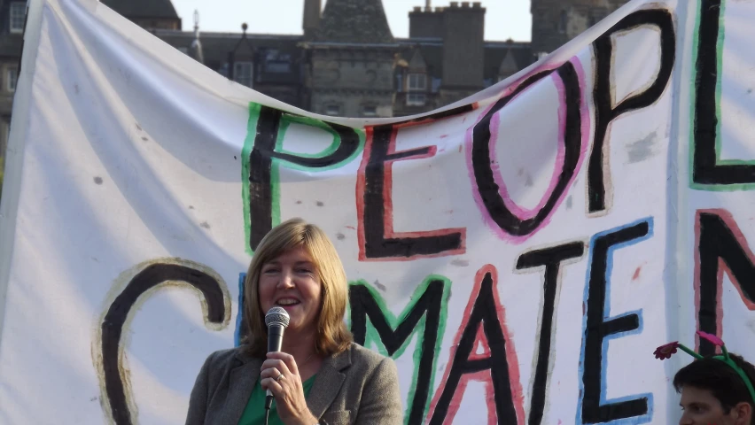 a woman speaking into a microphone in front of a political banner