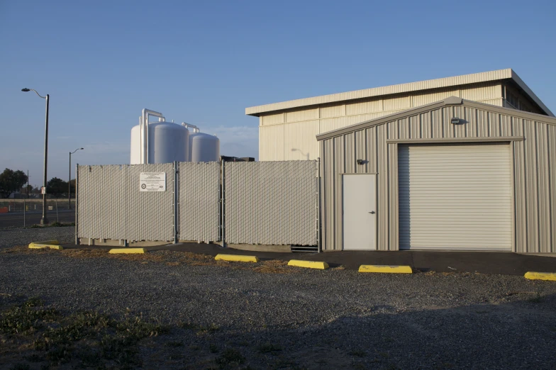 a small industrial shed is seen through a fence