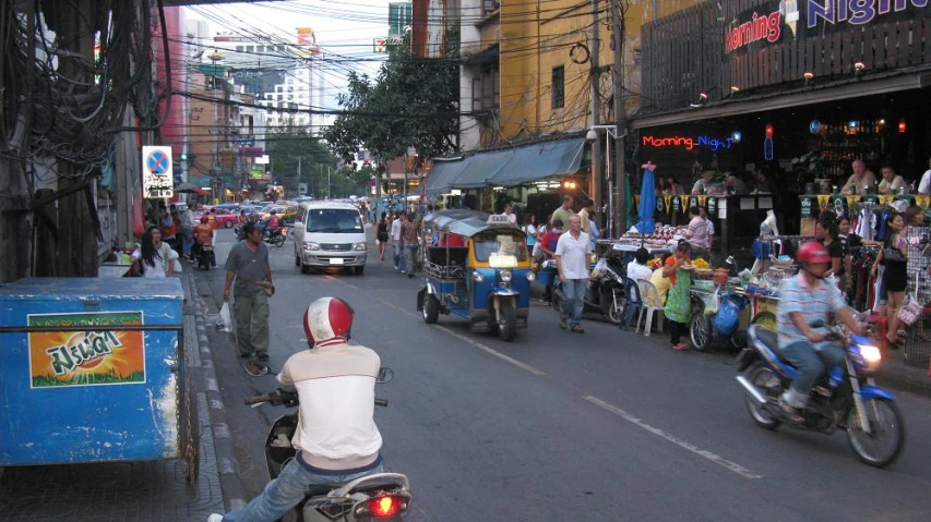 many people on motorcycles passing down the street with cars