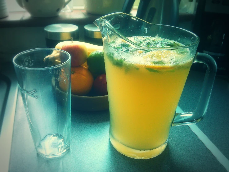 pitcher on a table with a bowl of fruit and a glass of soda