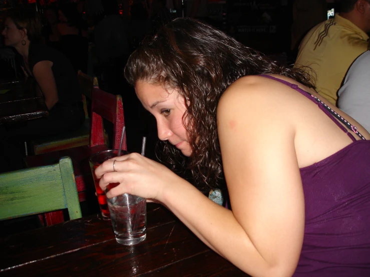 a woman in a purple tank top sits at a table with a glass