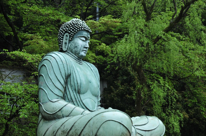 a statue of buddha sitting in a park with many trees