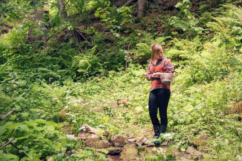 a young woman standing in a forest with a frisbee