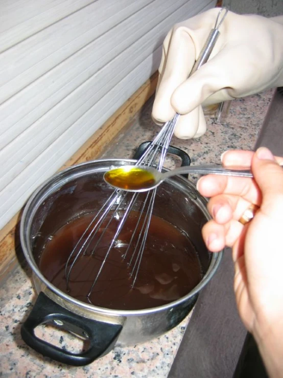 a hand stirring a sauce in a pot with tongs