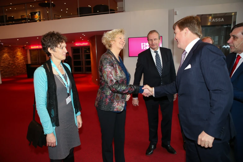 a group of people in suits shake hands in front of a large tv