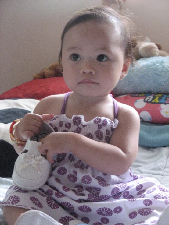 a small child sits in her bed with some white shoes