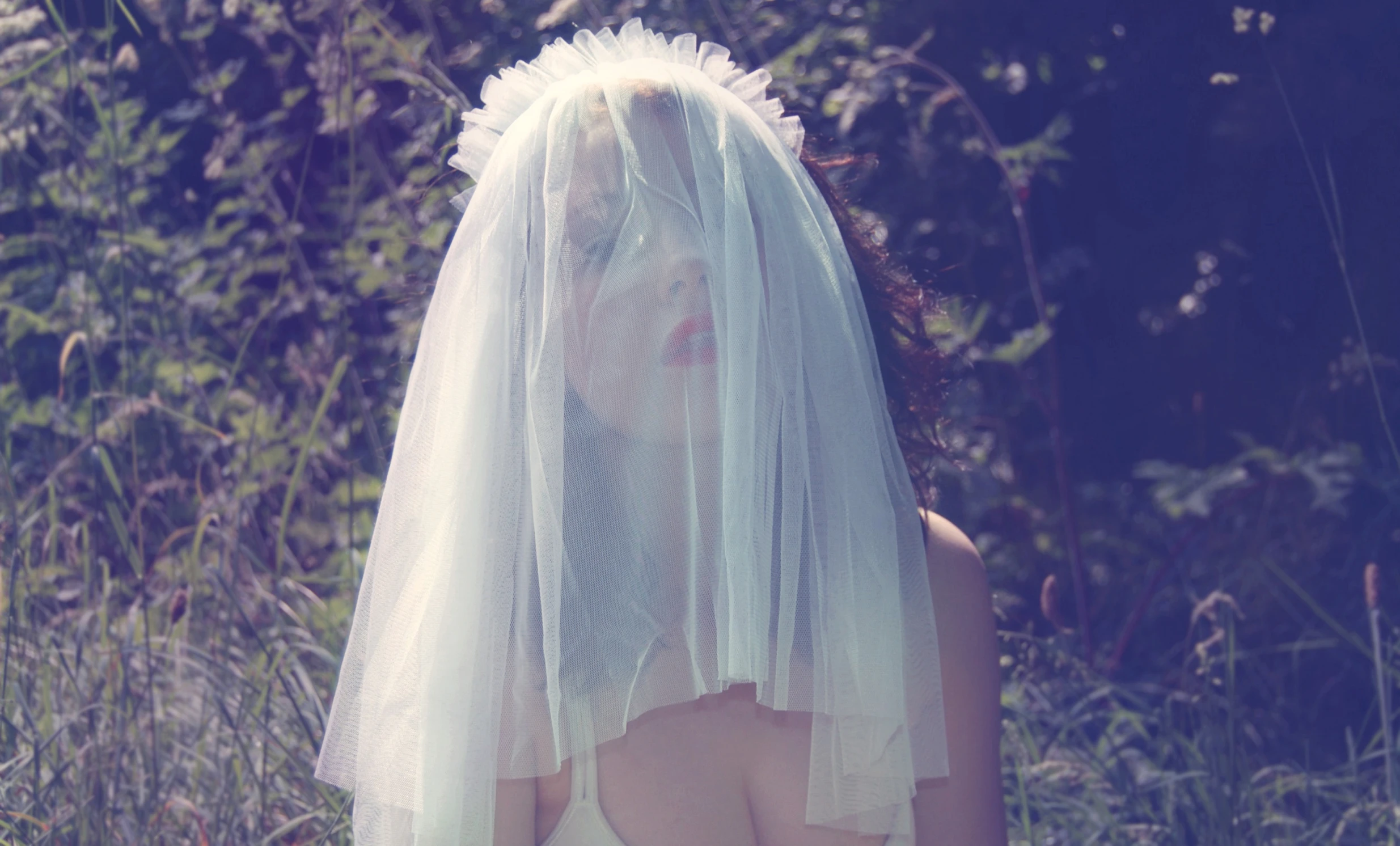 a bride in white veil walking through a field