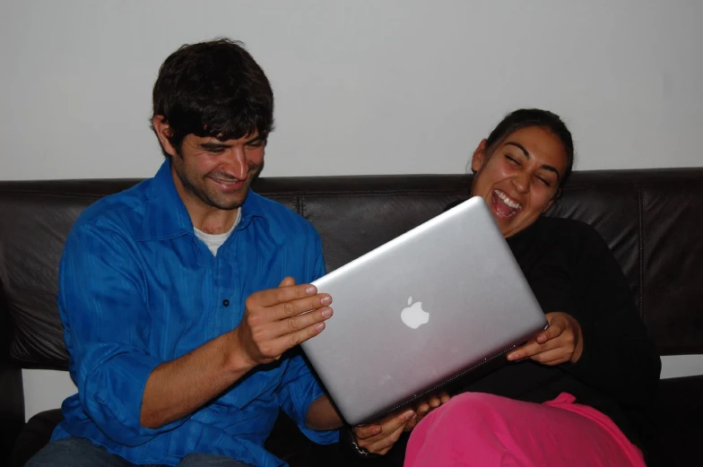 a man and woman laugh while looking at their laptop