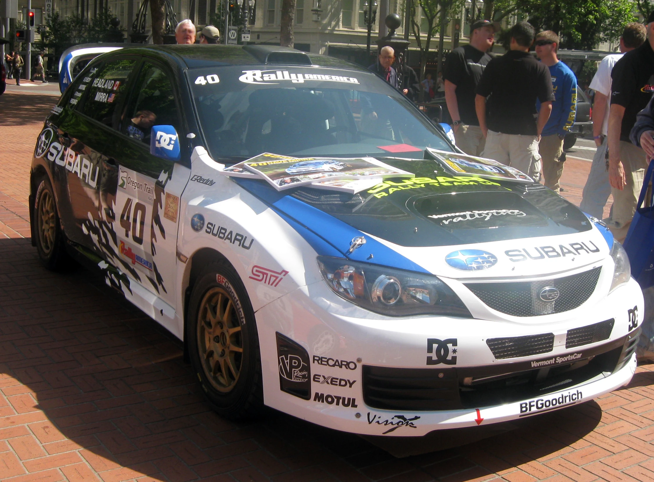 a subaru racing car is on the street during some people