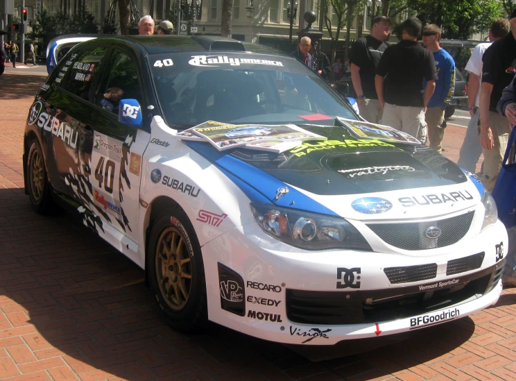 a subaru racing car is on the street during some people