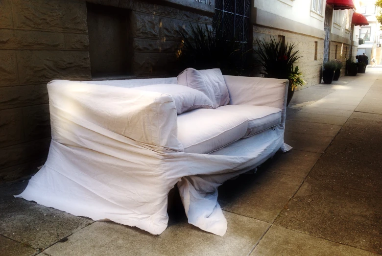 a sofa covered with a sheet on the sidewalk