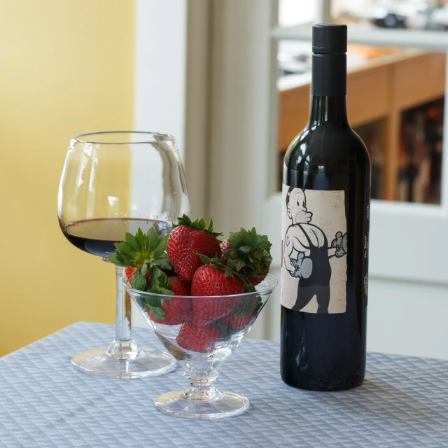 a glass filled with strawberries next to a bottle of wine