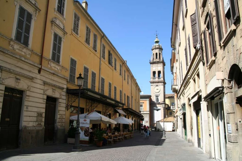 a narrow city street with some people sitting at tables on the side