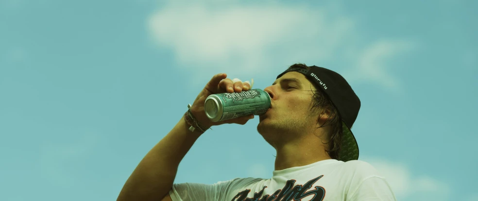 a man drinking a beer while wearing a hat