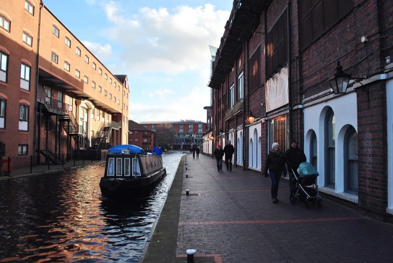 people walking in the street near a waterway that has a small boat