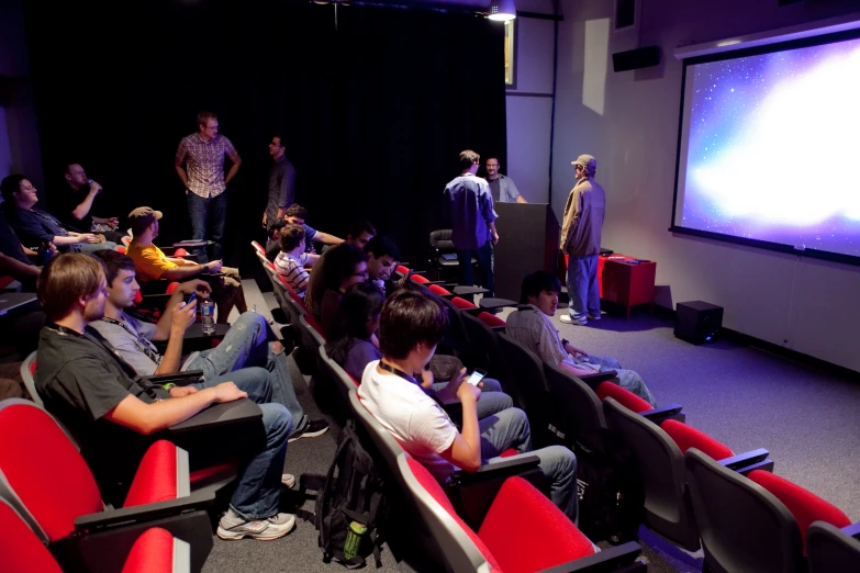 several people in an auditorium watching soing on the screen