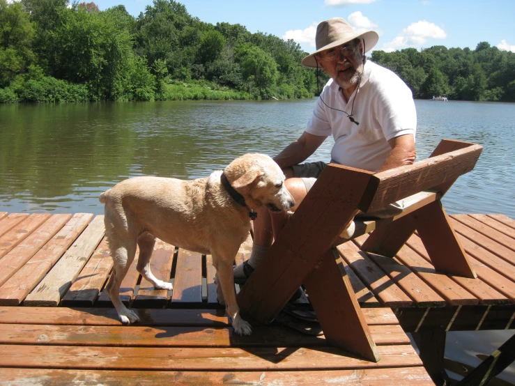 a man sitting next to a dog near a lake