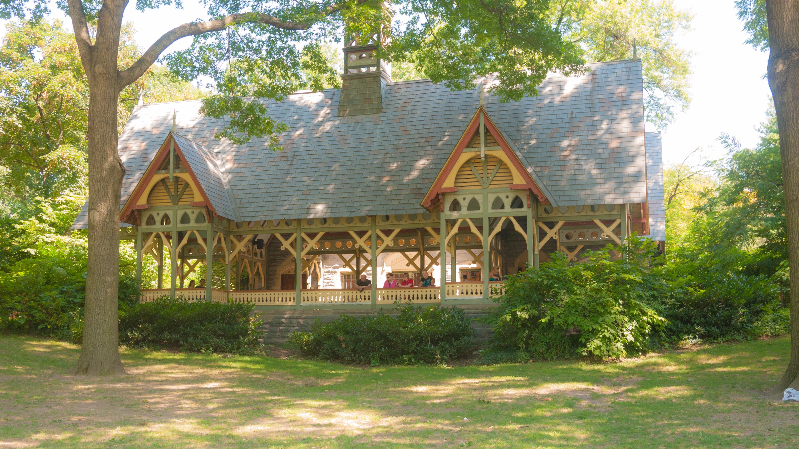 an old building with a porch and gable roofs surrounded by grass and trees