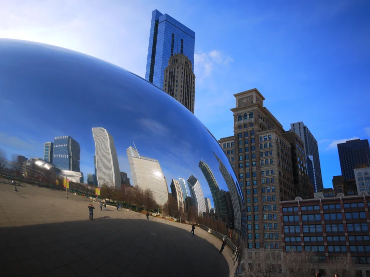 a shiny steel sculpture with some buildings in the background