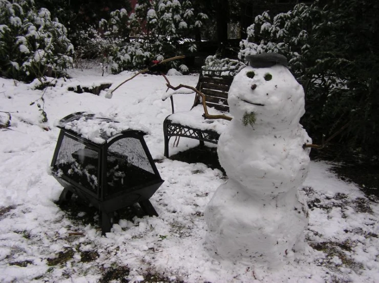 a snowy dog house next to a snowman sitting in the grass