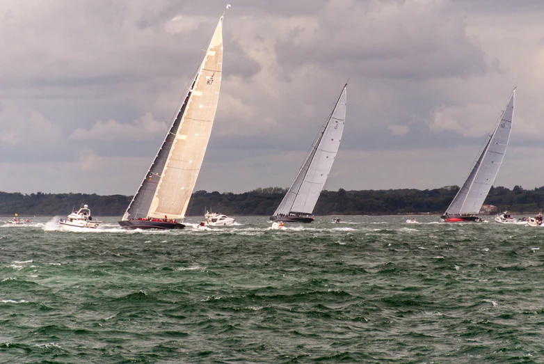 three sail boats racing in the ocean near each other