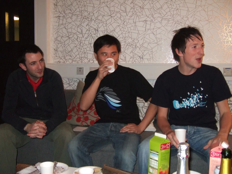 three men sitting on couches, one holding a game controller