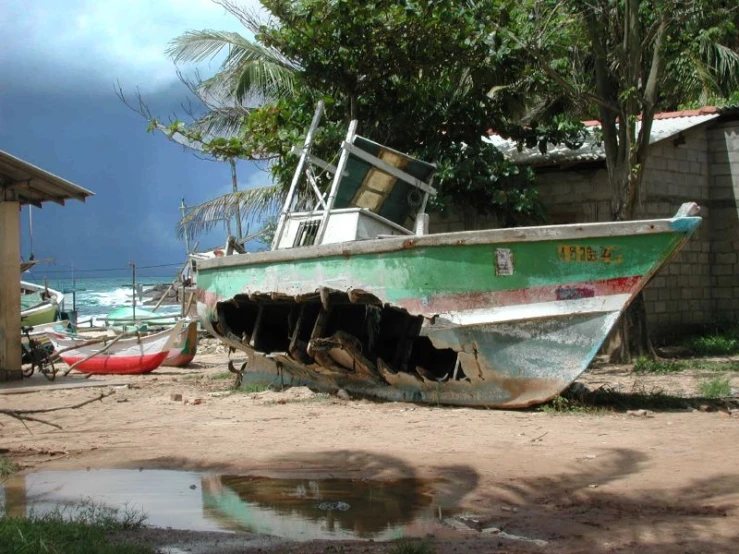 a dirty, green boat rests in the sand near a fence