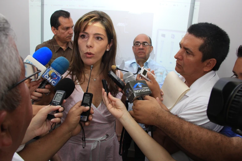 a woman surrounded by microphones talks to several other people