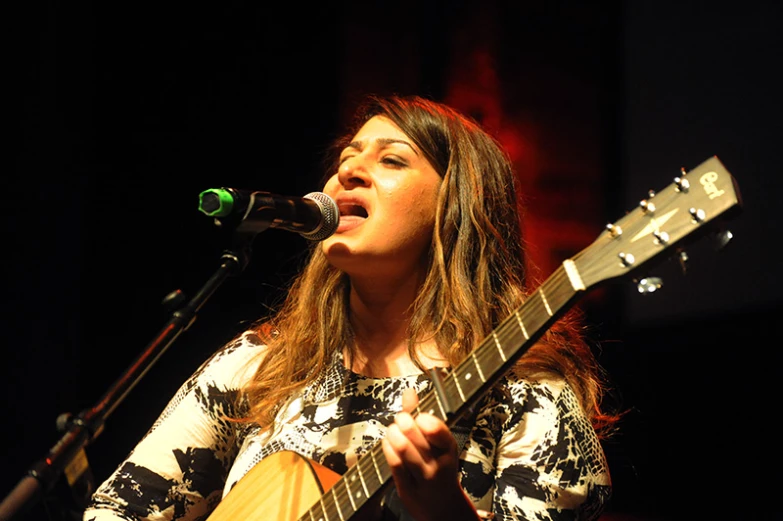 a woman with long hair playing a guitar and singing into a microphone