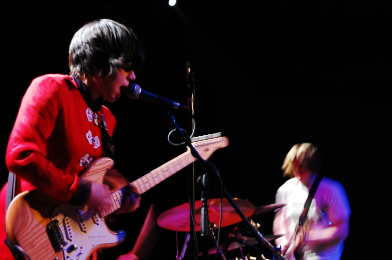 a man playing guitar in front of another man with a microphone