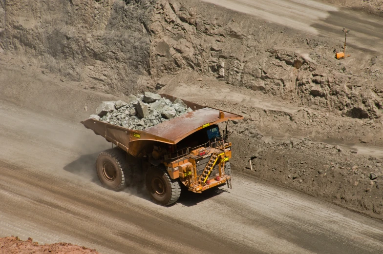 a dump truck with rocks on its side driving through some dirt