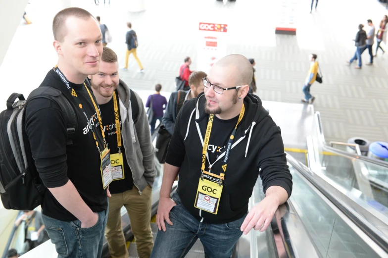 three men are looking at soing while standing next to an escalator