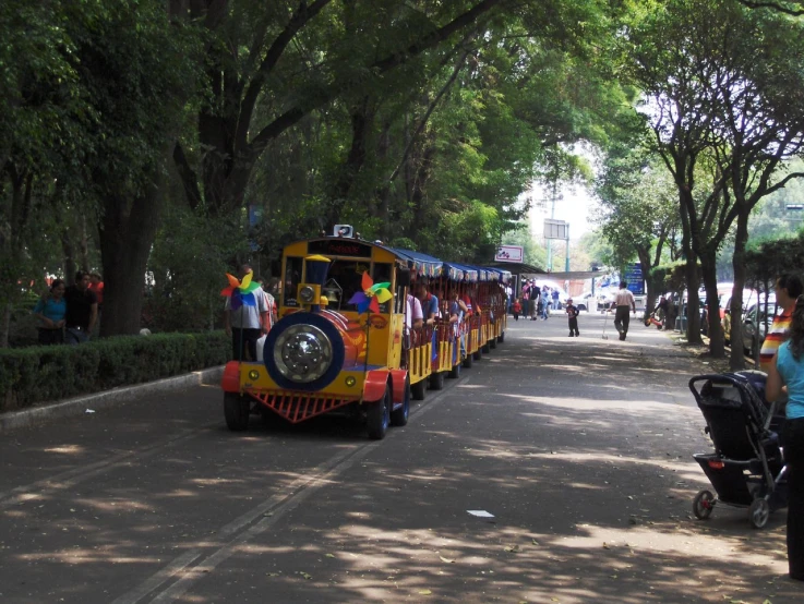 a child's train drives down the street as adults look on