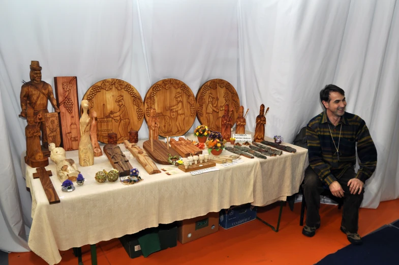 the man is sitting at the table with many wooden carved sculptures