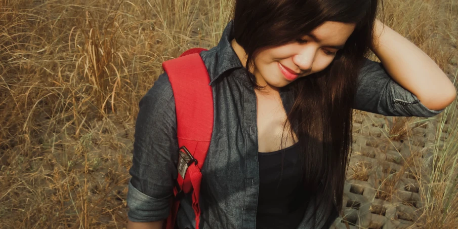 a person with long hair with a backpack in front of a field