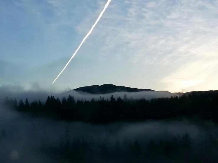 the sky is foggy and the mountain with trees