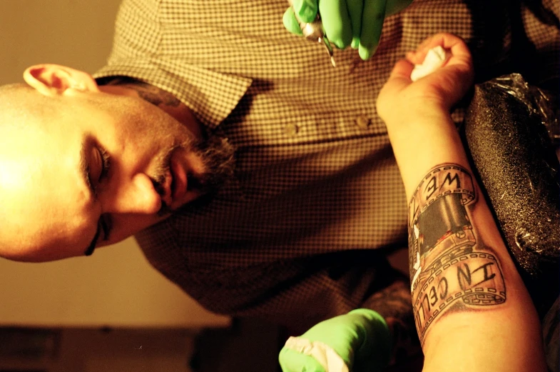 man holding bunches of green bananas while getting ink on his arm
