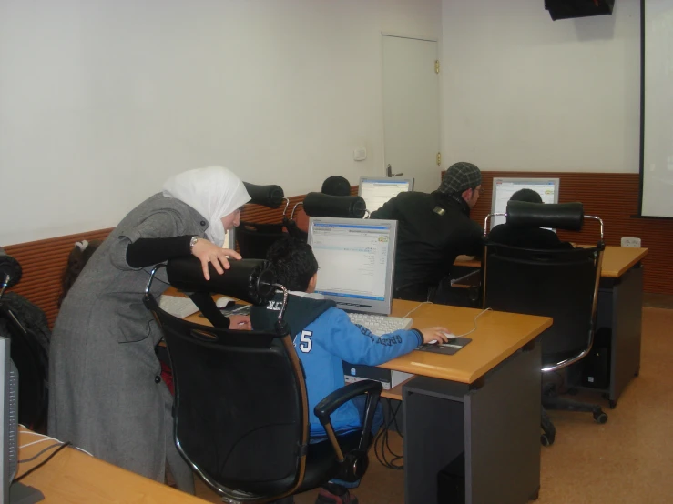 two people sit at desks with computers in an office