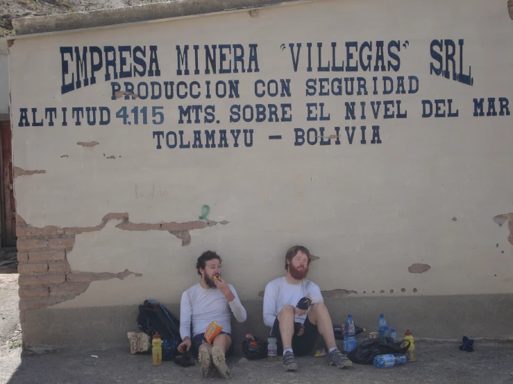 two men sitting in front of a sign on a wall